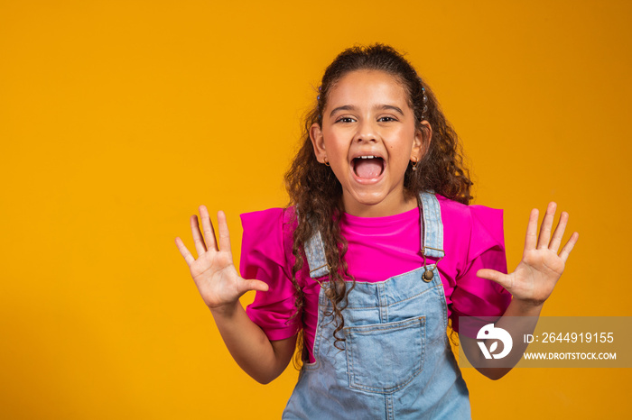 Beautiful girl child call somebody hold hands near face, isolated over yellow studio background wall, emotional small pretty kid open mouth look at camera shout speak loud make announcement concept.