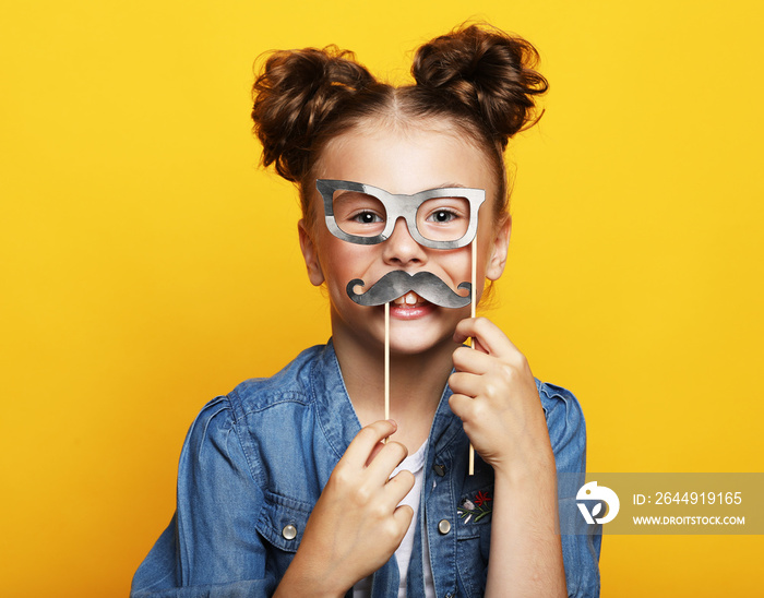 Party, childhood and people concept: little girl with a paper accessories over yellow background.