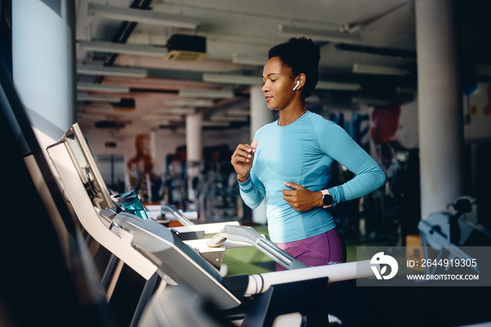 Black female athlete running on treadmill while exercising in gym.
