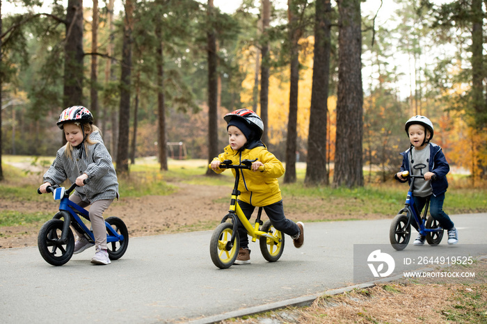 Two little boys and blond girl riding their balance bikes in park