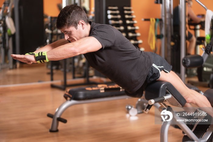 Lower back exercises for strengthening the muscles for spine health. Fitness man doing superman exercise workout with arms raised on gym bench. Bodyweight training .