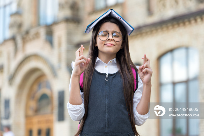 Crossing fingers for luck. Little geek make wish outdoors. Small child hold book on head. Knowledge day. September 1. School library. Primary education. General knowledge. Absorbing the knowledge