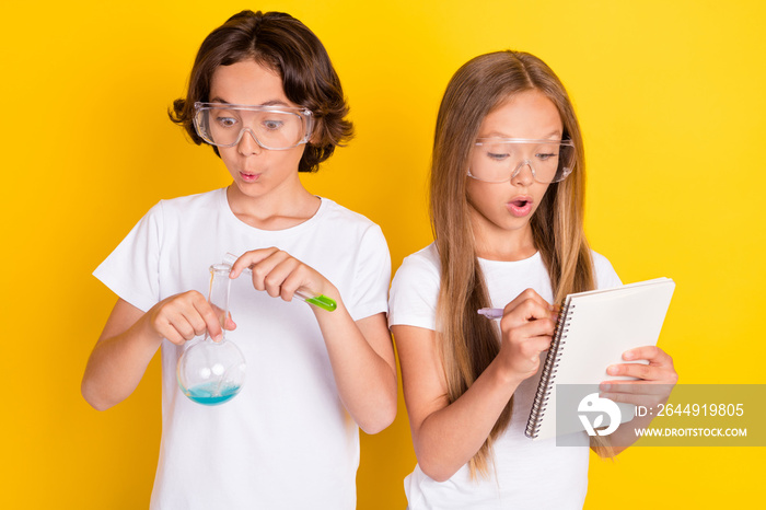 Portrait of two attractive amazed kids learning chemistry lab subject writing note isolated over bright yellow color background