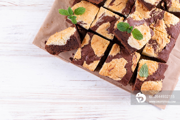 Chocolate brownie square pieces with cookies, decorated with mint leaves on a wooden table. Place for text