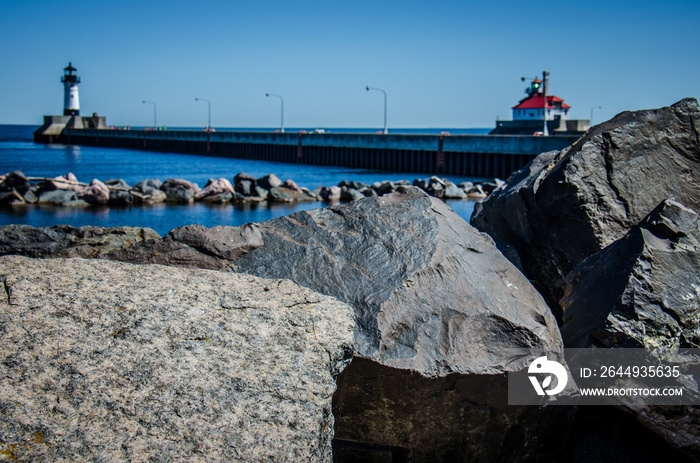 Focus on giant rocks with intentionally blurred Canal Park Lighthouse, also known as South Breakwater Light in Duluth Minnesota on Lake Superior