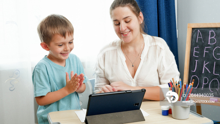 Smiling happy boy studying and learning on tablet computer with young smiling mother. Home education and remote school, Doing homework on tablet computer