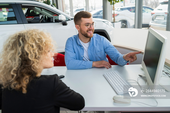 Car dealership manager with client at computer in showroom