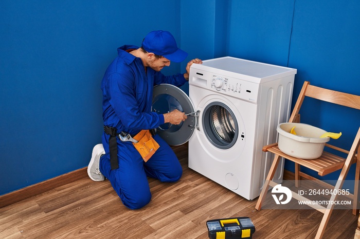 Young hispanic man technician repairing washing machine at laundry room