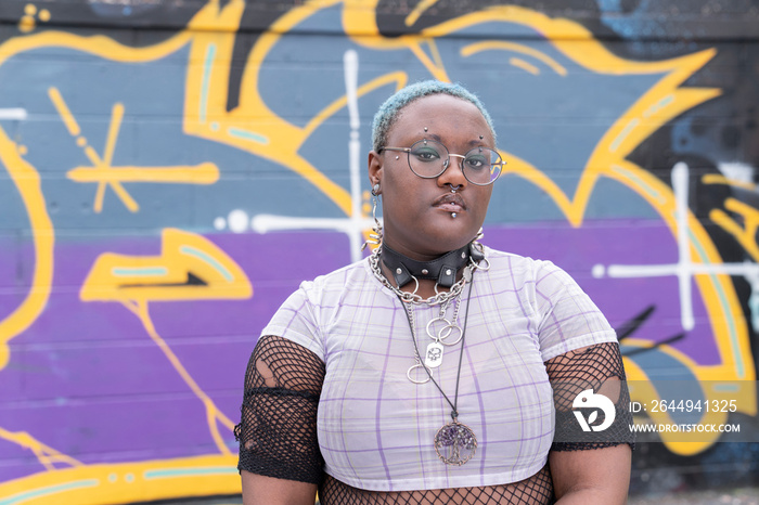 Portrait of serious non-binary person against graffiti wall