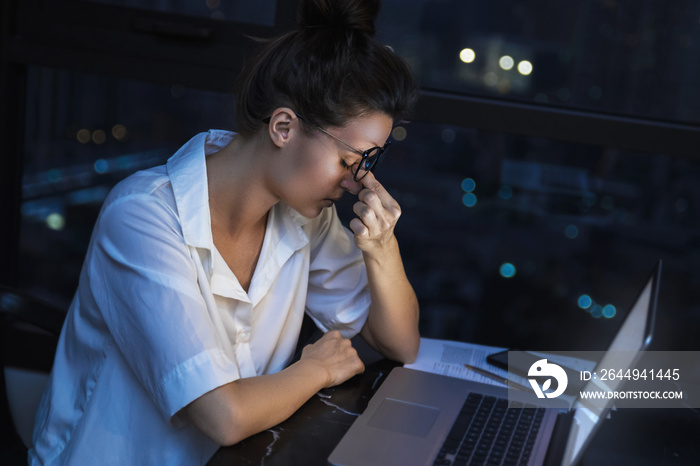 Woman is working with laptop at home during night.