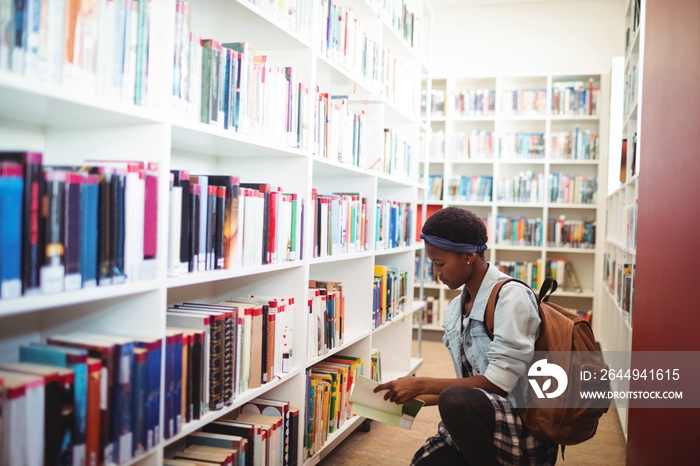 Schoolgirl selecting book from book shelf in library