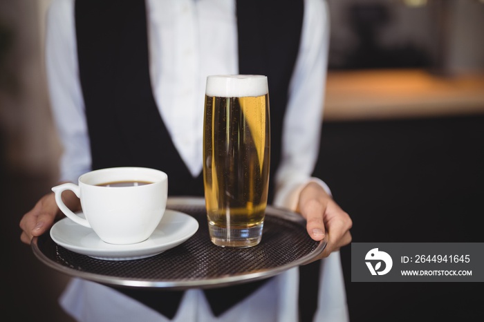 Mid-section of waitress holding tray with coffee and beer glass