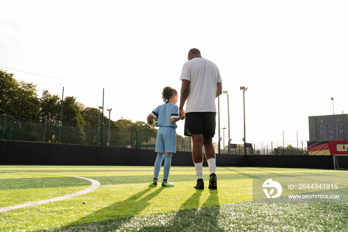 Rear view of coach and girl (6-7) on soccer field