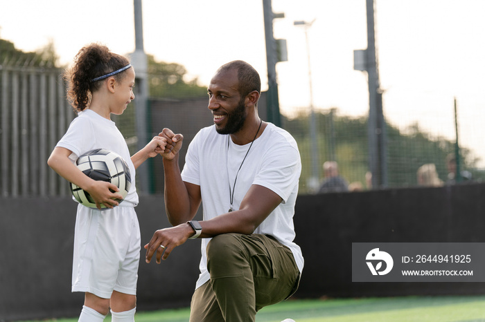 Man instructing girl (6-7) with ball on soccer field