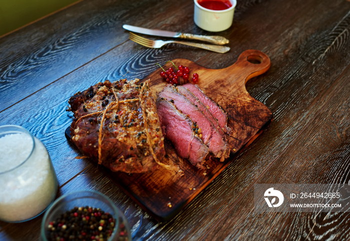 Appetizing veal tenderloin baked in the oven until  blue rare, the cook served on a cutting board, standing next to the sauce to the meat of wild berries