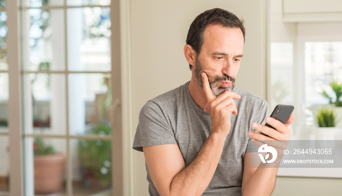 Middle age man using smartphone serious face thinking about question, very confused idea