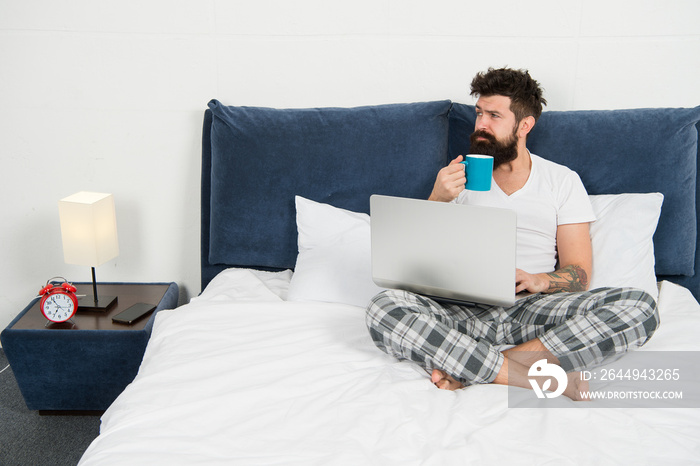 Hipster bearded guy pajamas freelance worker. Remote work concept. Social networks internet addiction. Online shopping. Man surfing internet or work online. Just woke up and already at work