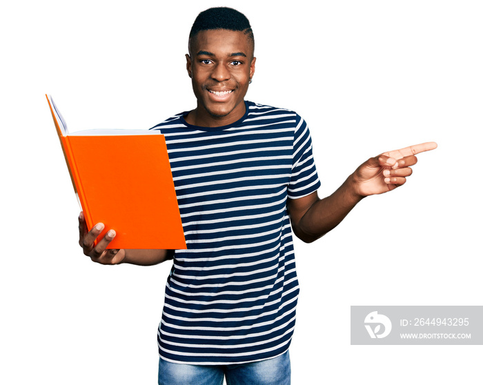 Young african american man holding book smiling happy pointing with hand and finger to the side