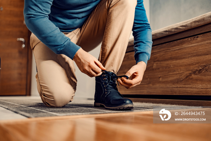 A man in shoes or boots. A man is kneeling at home, tying his shoelace, and preparing to go outside.