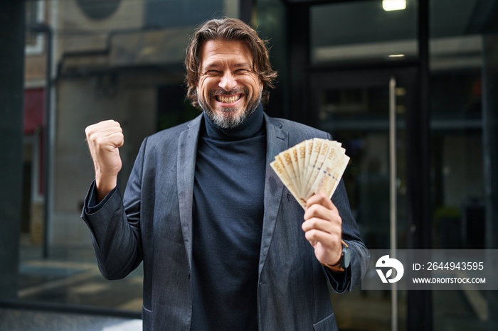 Handsome middle age man holding 100 danish krone banknotes screaming proud, celebrating victory and success very excited with raised arm