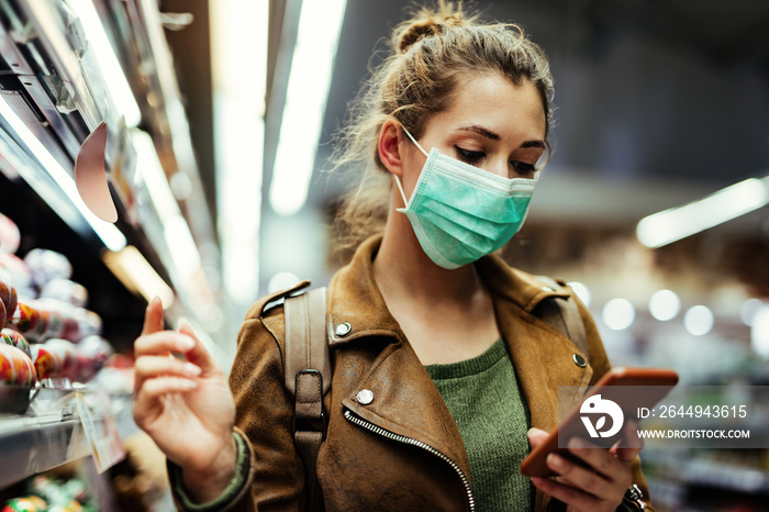 Woman with face mask going through check list on smart phone while buying in supermarket.