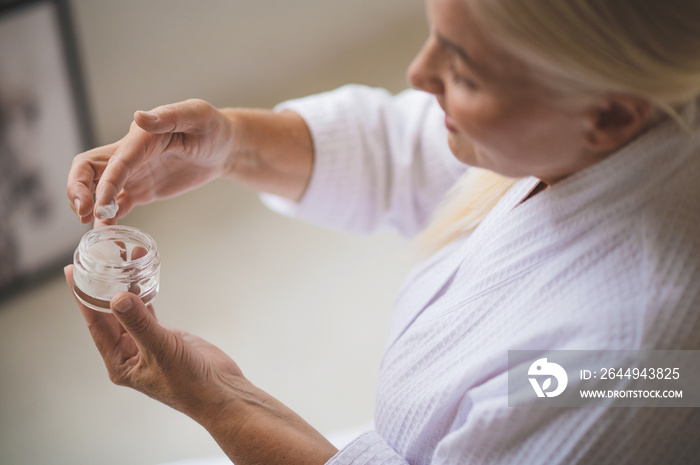 Pretty well-groomed woman applying cream on her face