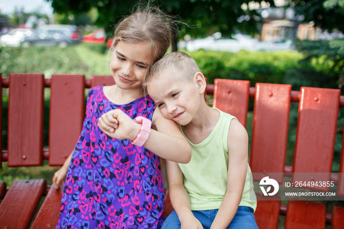 Happy kids sitting on bench and making photo with smartwatches with smile, parents control during walking, new technology for children, digital education and care, outdoors lifestyle