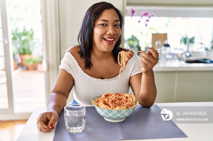 Hispanic brunette woman eating spaghetti at the kitchen