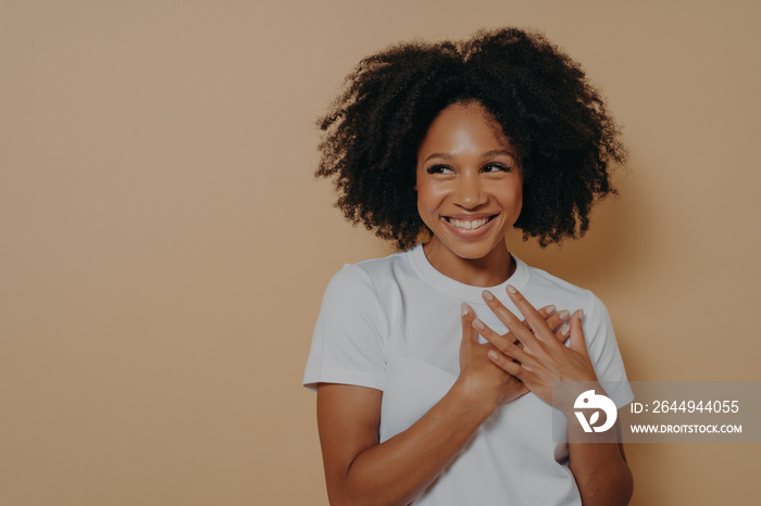 Portrait of happy african woman posing with smile looking away, holding hands on chest