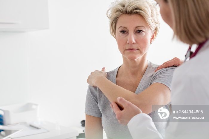 Doctor assisting mature patient in stretching her arm at hospital