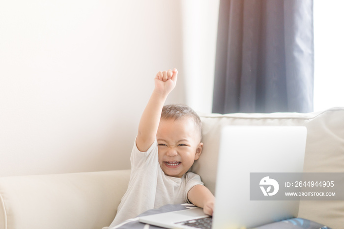 Portrait of a little toddler boy watching laptop and exciting face.Little asian boy child with laptop computer or notebook in living room at home.E Learning, Shopping online concept.