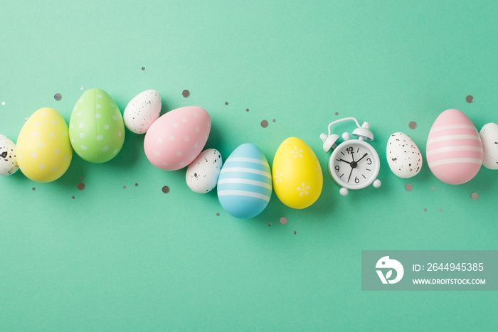 Top view photo of easter decorations glowing confetti row of multicolored easter eggs and white alarm clock on isolated turquoise background with copyspace