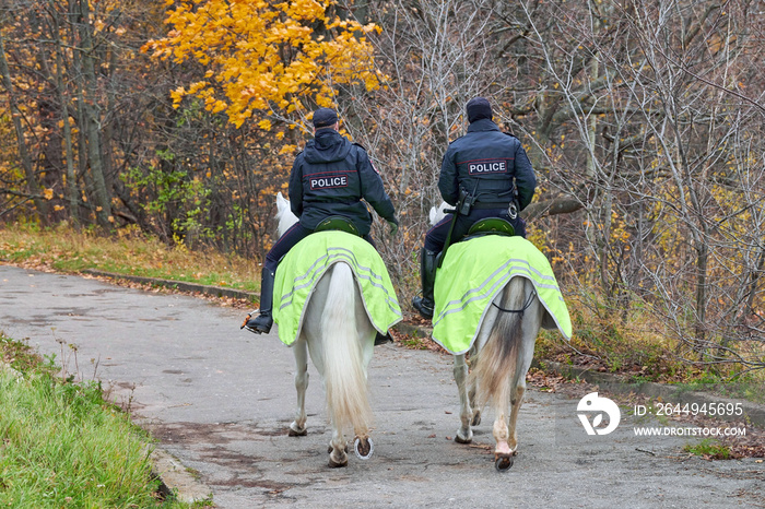 Mounted police in autumn city park, back view