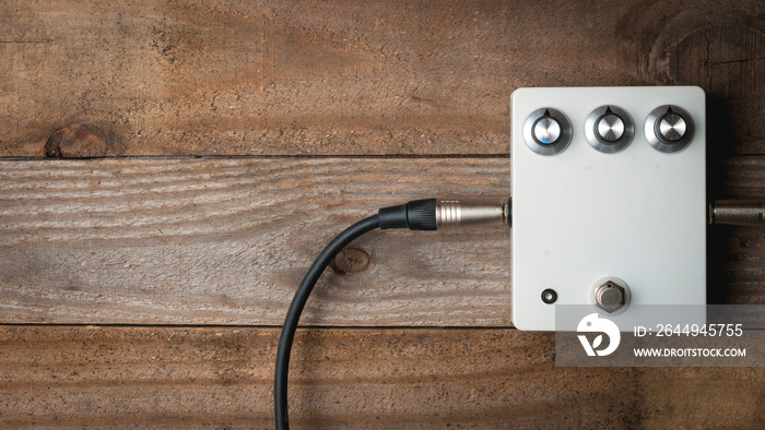 Blank white guitar pedal with vintage knobs and plugged jacks on wooden floor