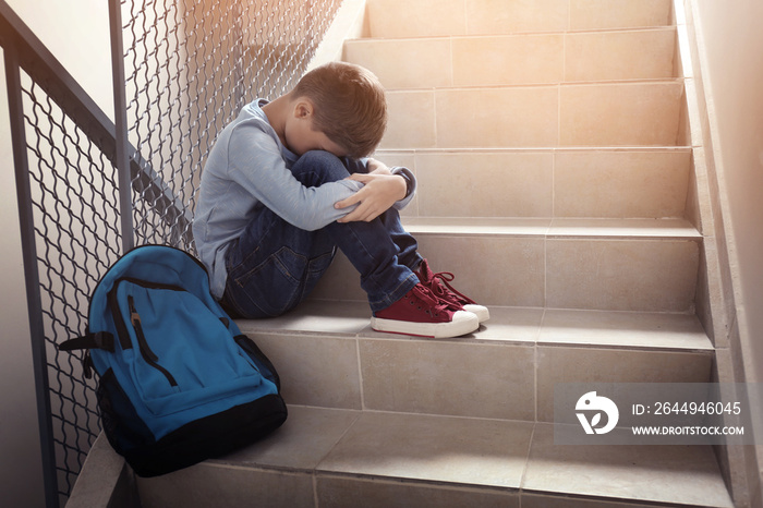 Upset little boy sitting on stairs indoors