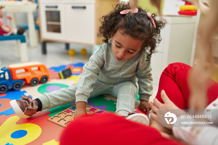 Adorable hispanic girl playing with maths puzzle game sitting on floor at kindergarten