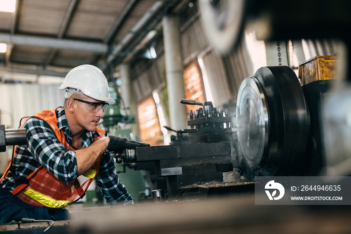 worker is working on a lathe machine in a factory. Turner worker manages the metalworking process of mechanical cutting on a lathe