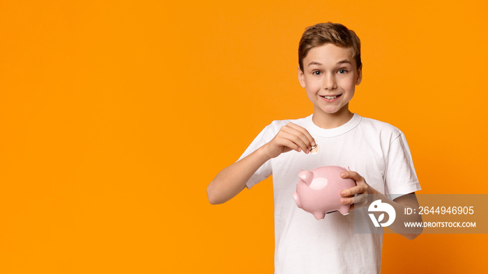 Smiling little boy putting money into piggy bank