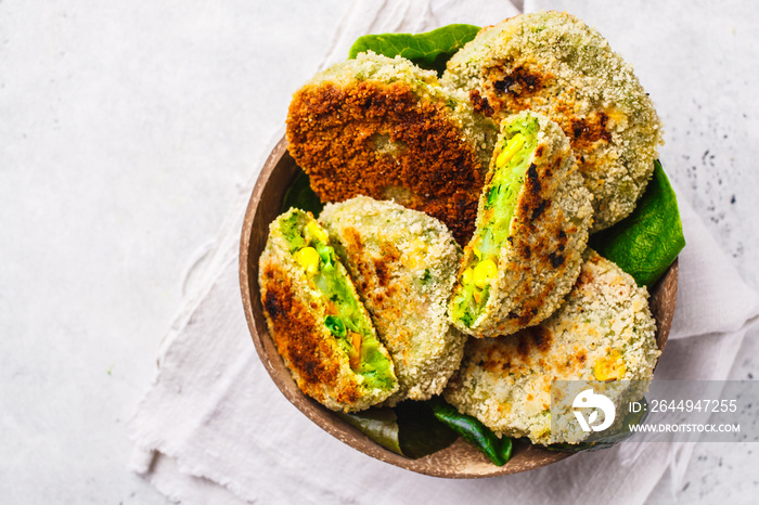 Green vegetarian burgers in coconut shell dish on white background.