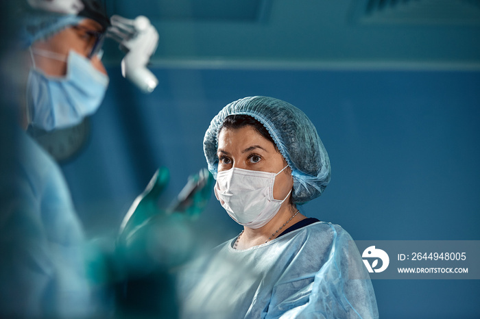 Two surgeons in protective uniform during the operation, on background of surgical room. Point of view shot
