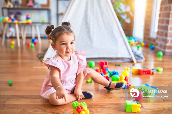 Young beautiful toddler sitting on the floor playing with building blocks at kindergaten