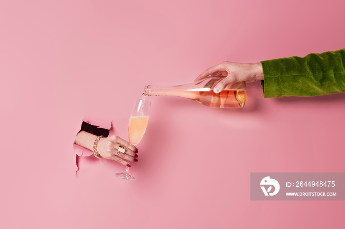 Partial view of woman holding glass near man with bottle of champagne and pink background with hole