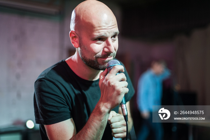 Smiling and witty stand up actor comedian on stage, talking and singing