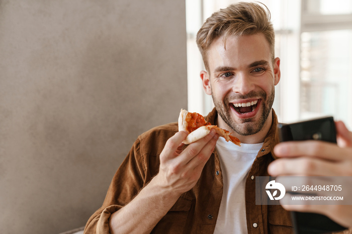 Man eating pizza while talking by videocall by mobile phone