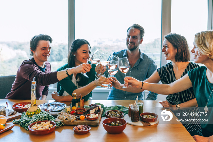 Friends rising wine glasses for a celebratory toasting at home sitting a party table full of finger food