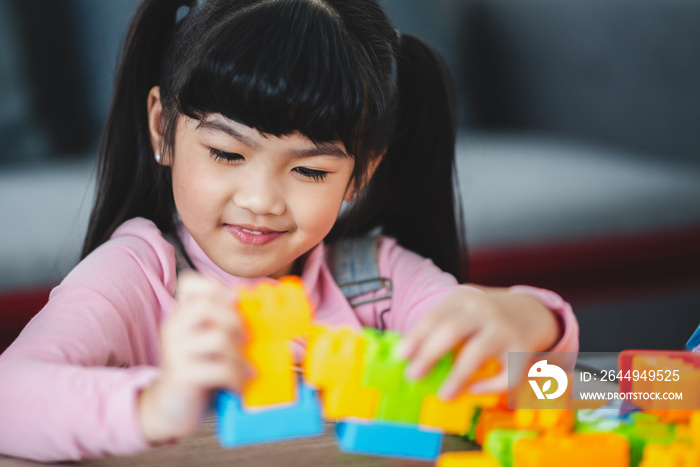 Cute little Asian girl playing alone with lego game blocks on table trying to build a new object while relaxing and enjoying