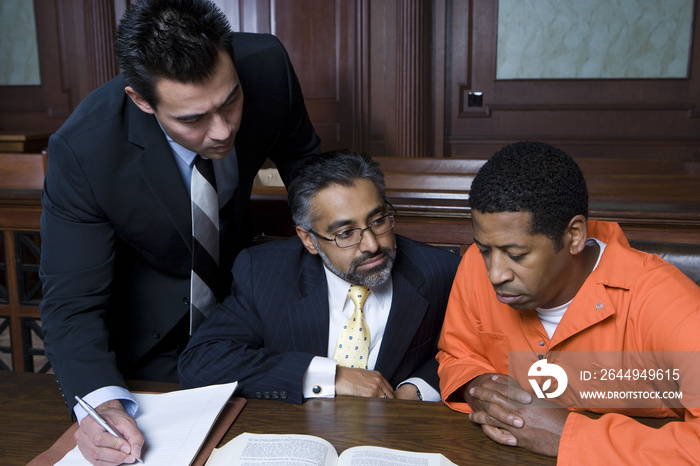 Criminal sitting with two lawyers in the courtroom
