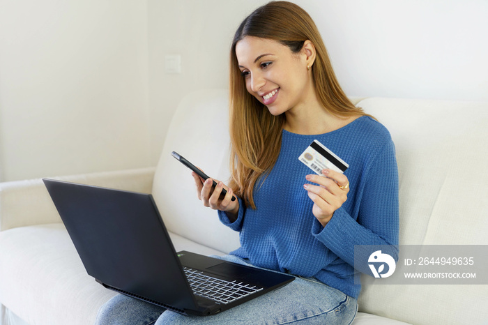 Brazilian woman holding credit card and smartphone using laptop computer for online shopping at home. OTP, two-factor authentication, pix and token for paying online concept.