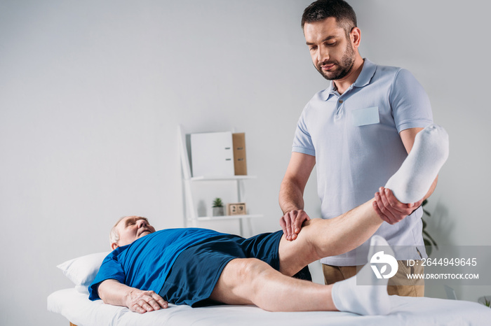 focused rehabilitation therapist massaging senior mans leg on massage table