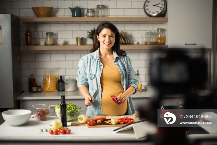 Beautiful pregnant woman filming cooking vlog. Happy woman filming her blog about healthy food at home